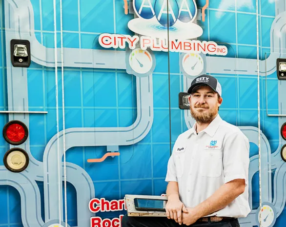 A plumber in uniform stands holding a tool in front of a service van with the AAA City Plumbing Inc. logo and blue pipe graphics.